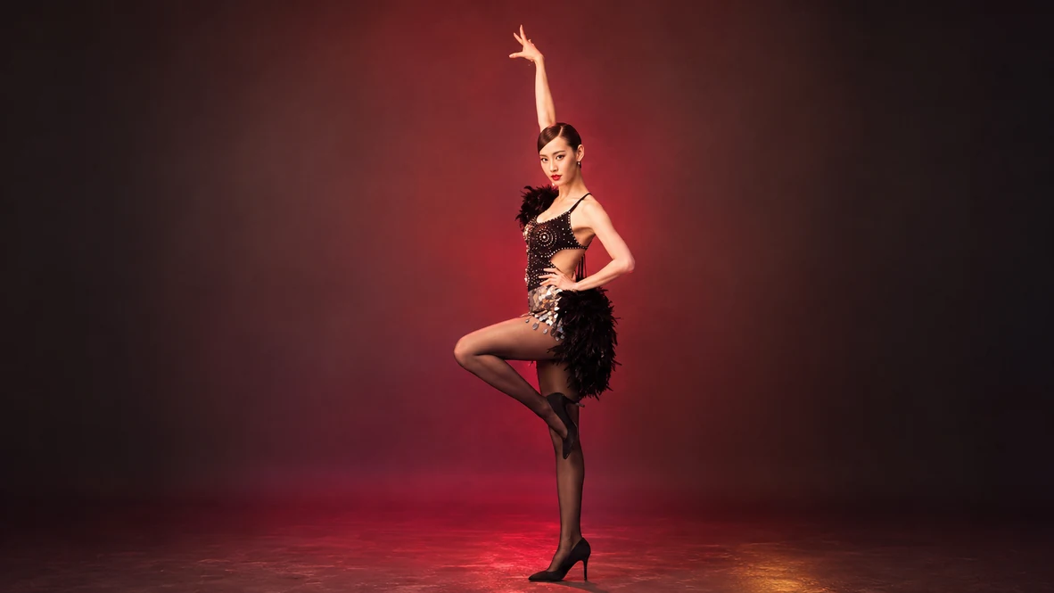 Showgirl dancer in a black feathered costume under warm red and golden stage lighting